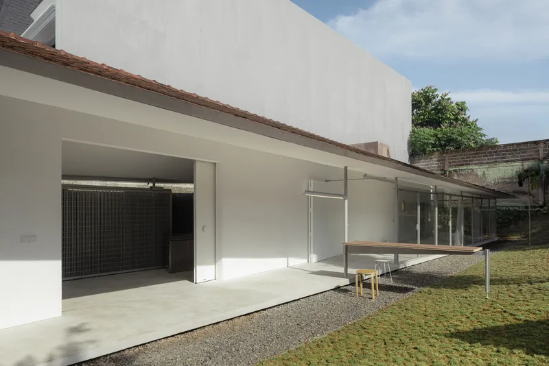 White-rendered facade with glass doors opening to a gravel courtyard and lawn under blue sky