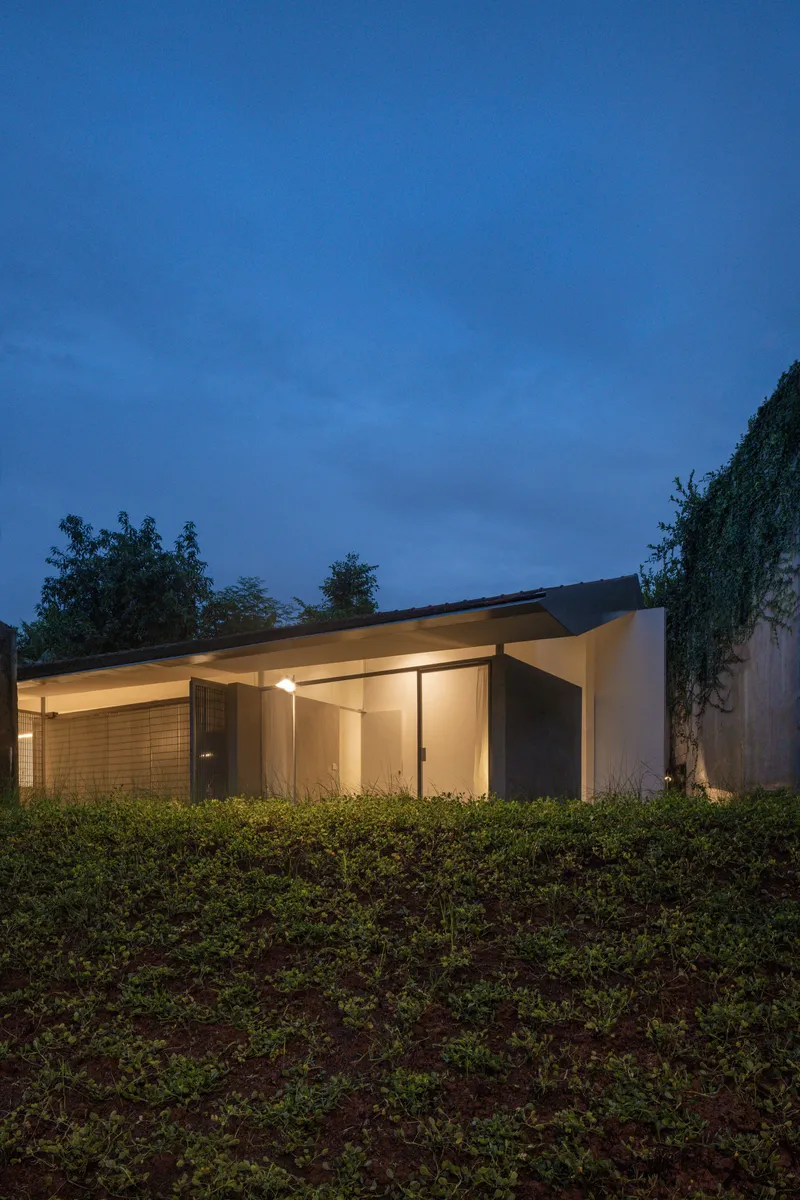 Low-slung folded roof structure nestled into hillside vegetation at dusk