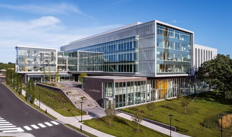 Elevated view of the translucent panel facade and glass curtain wall rising above landscaped lawn and approach road