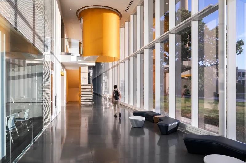 Double-height lobby with cylindrical yellow volume and polished concrete floor as figure walks past angular seating