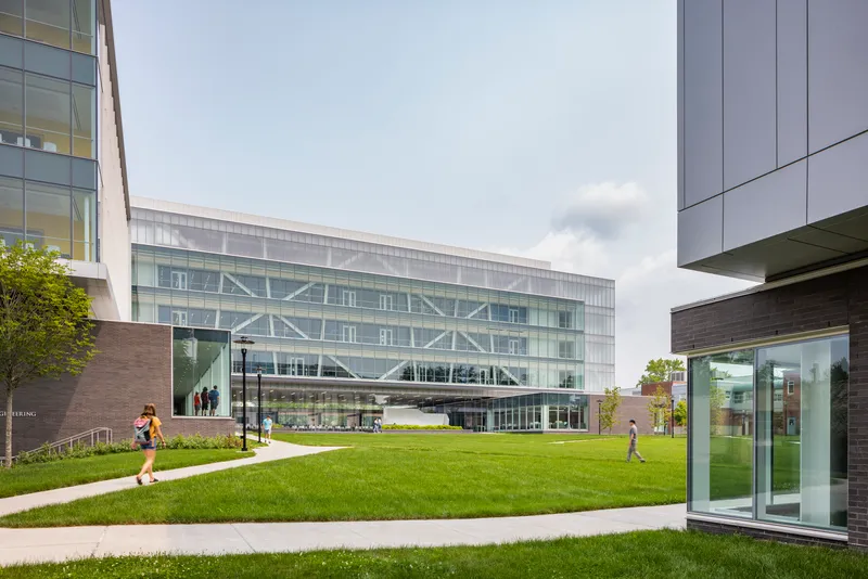 Diagonal braced facade visible through translucent panels as students cross the green lawn