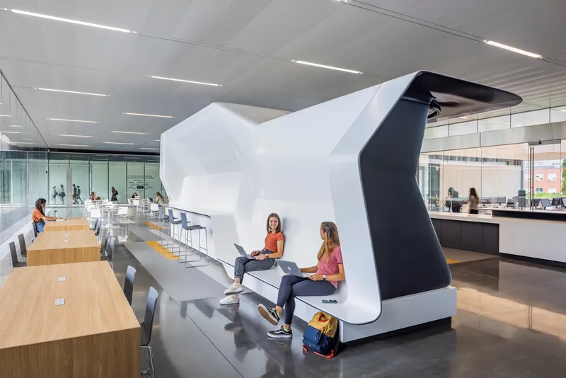 Sculptural white and black seating pod in a communal space with students gathered around tables