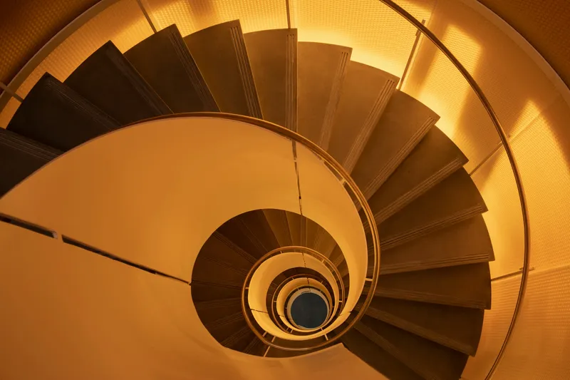 Top-down view of a spiral staircase with timber treads and metal handrail under warm lighting