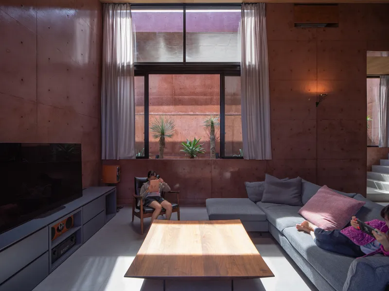 Living room with rammed earth walls and a high window framing potted plants in an exterior courtyard
