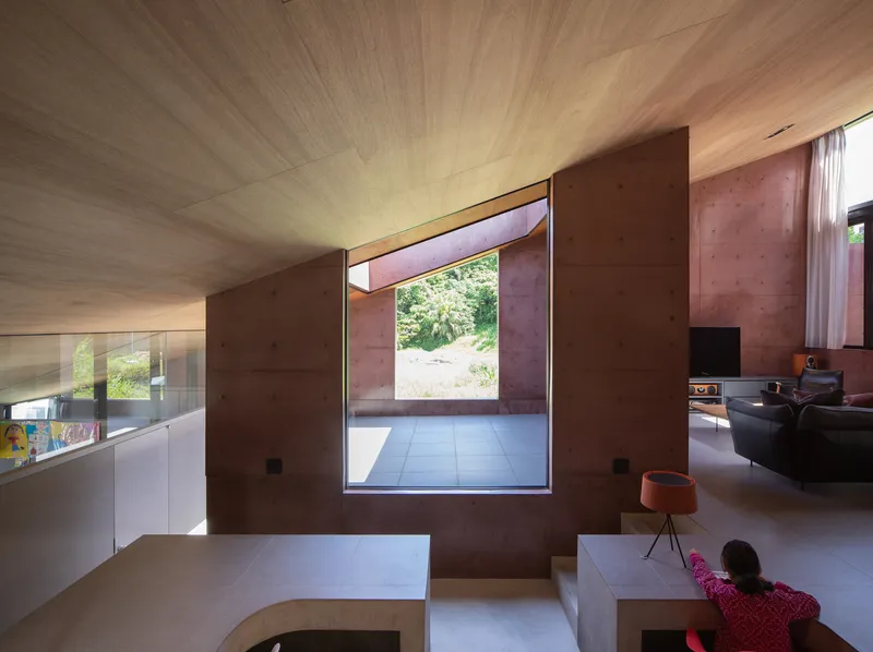 Interior space with vaulted wood ceiling and a framed opening looking through rammed earth walls to greenery