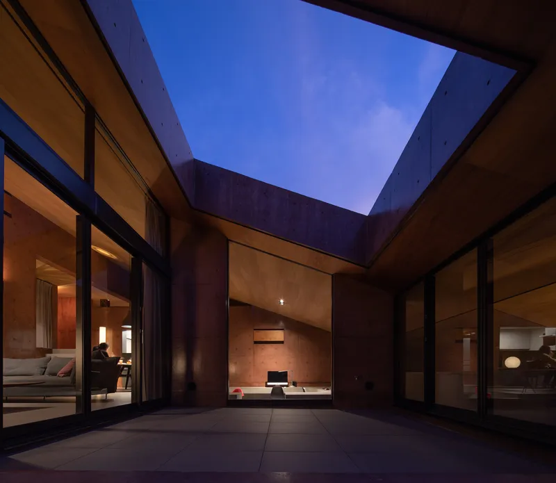 Interior courtyard framed by concrete walls and glass doors at twilight with a purple sky overhead