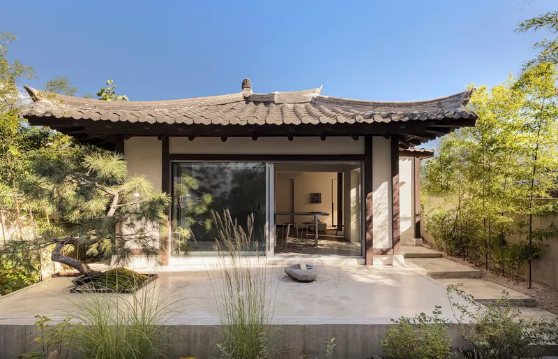 Pavilion with curved tile roof and timber columns opening onto a terrace with pine and bamboo