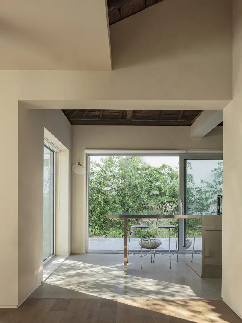 Interior corridor with dappled sunlight leading toward a glass-walled terrace and dining area