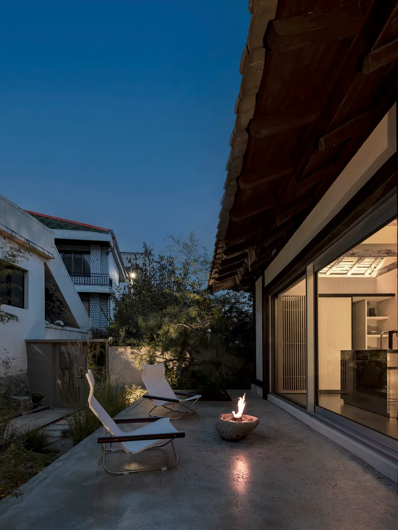 Courtyard terrace at dusk with fire bowl, lounge chairs and timber eaves above glazed walls
