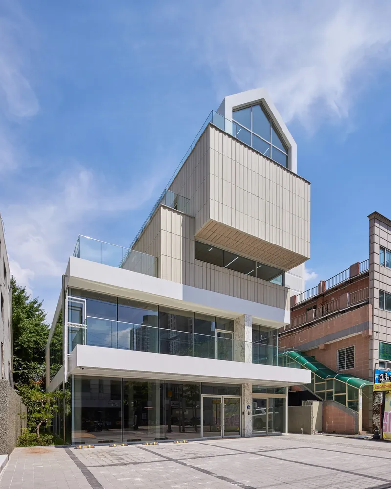 Street view of the stacked white volume facade with vertical metal cladding under a blue sky