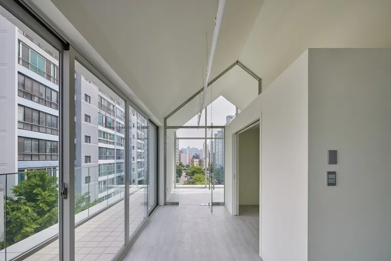 Interior corridor with floor-to-ceiling glazing along one side and pentagonal roof aperture framing daylight