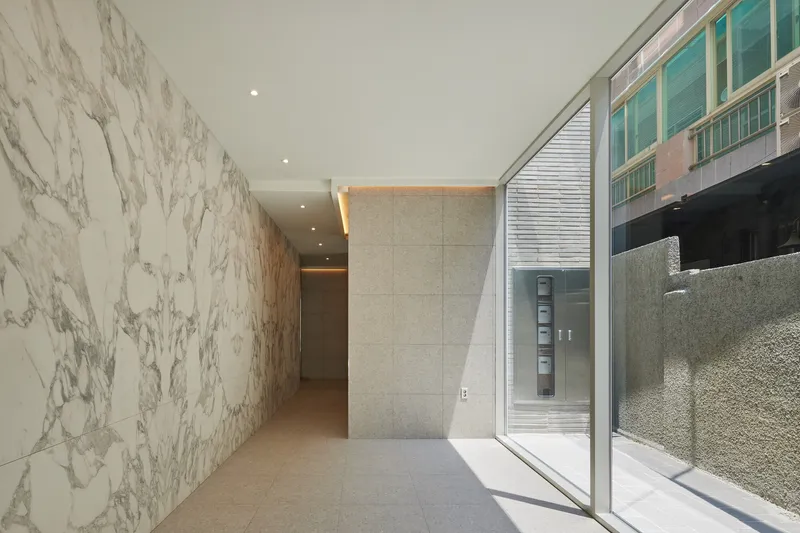 Entry hallway with white veined marble wall and glazed courtyard opening casting angular shadows