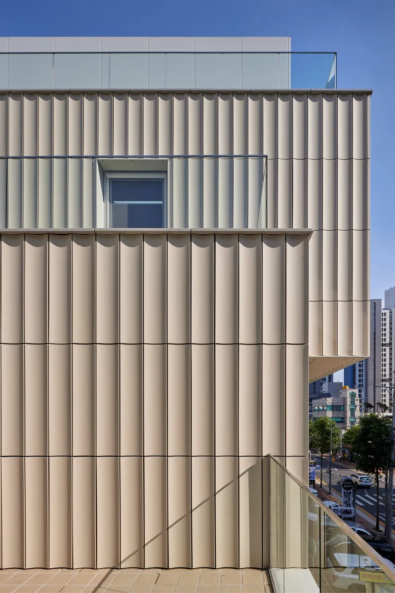 Facade with vertical ribbed beige panels and a single window opening under clear blue sky