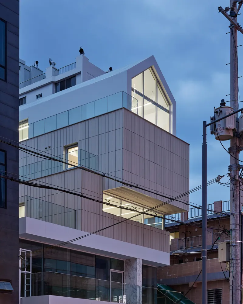 Stacked facade with vertical ribbed cladding and illuminated interiors at dusk with overhead power lines