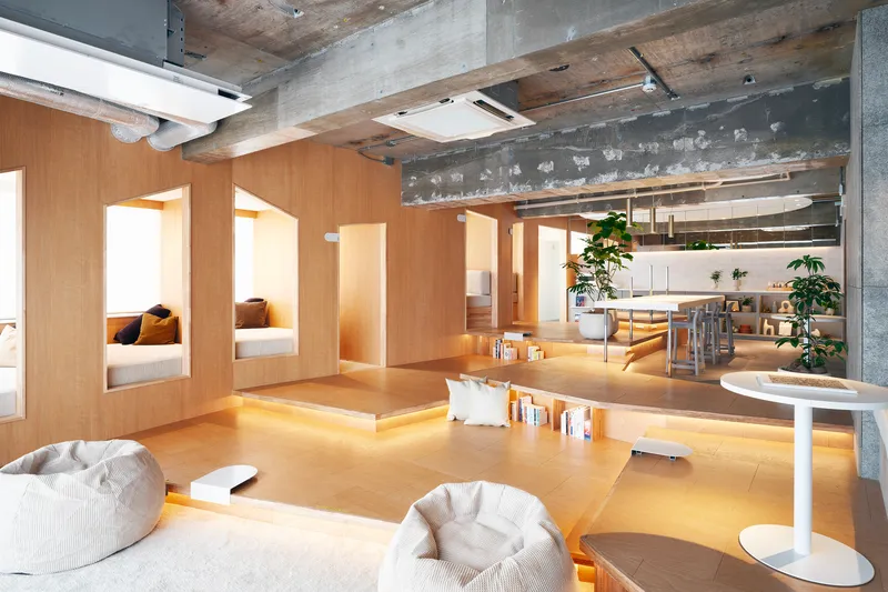 Open-plan interior with sunken plywood platform seating and exposed concrete ceiling beams