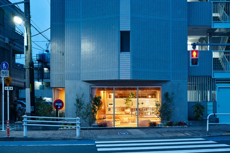 Street view of illuminated storefront with glass facade at dusk beside a crosswalk