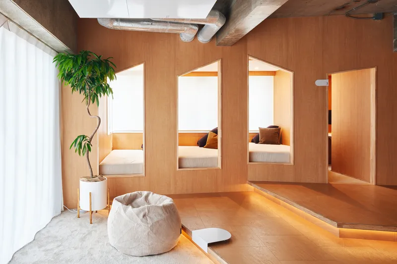 Three timber-framed sleeping nooks with built-in beds beside a white curtain and potted plant
