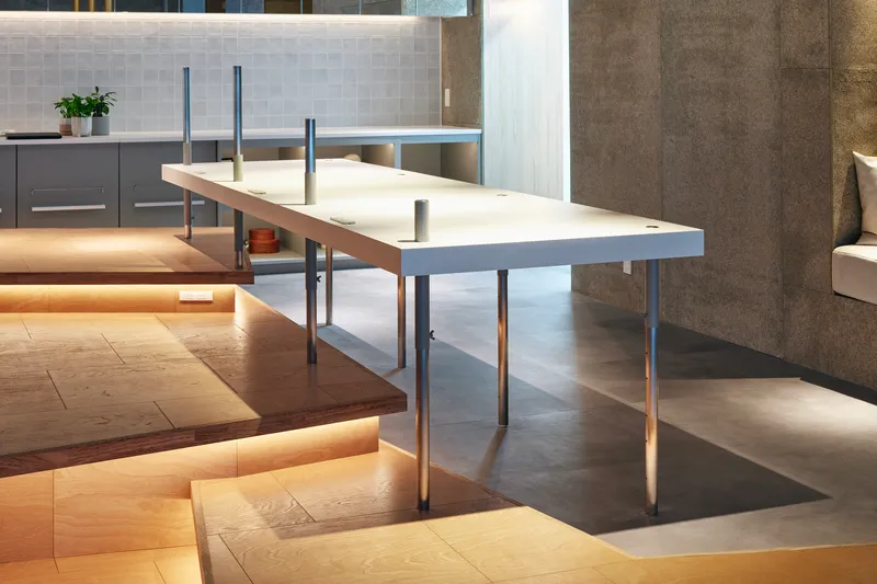 White composite table surface with metal and wood legs spanning across a stepped floor with hidden LED lighting