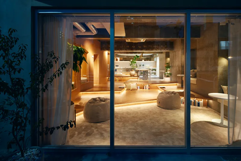 Exterior view at dusk showing the illuminated interior through full-height glazed sliding doors with a climbing plant to the left