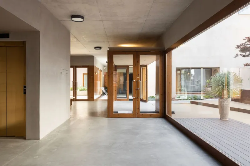 Entry lobby with timber-framed glass doors opening to a courtyard with wooden decking and palms