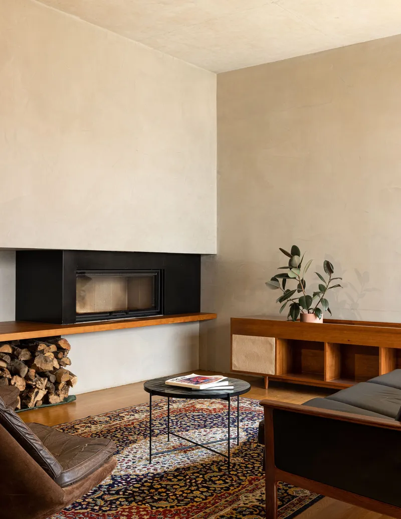 Living room with inset fireplace above stacked firewood and timber sideboard beside a patterned rug