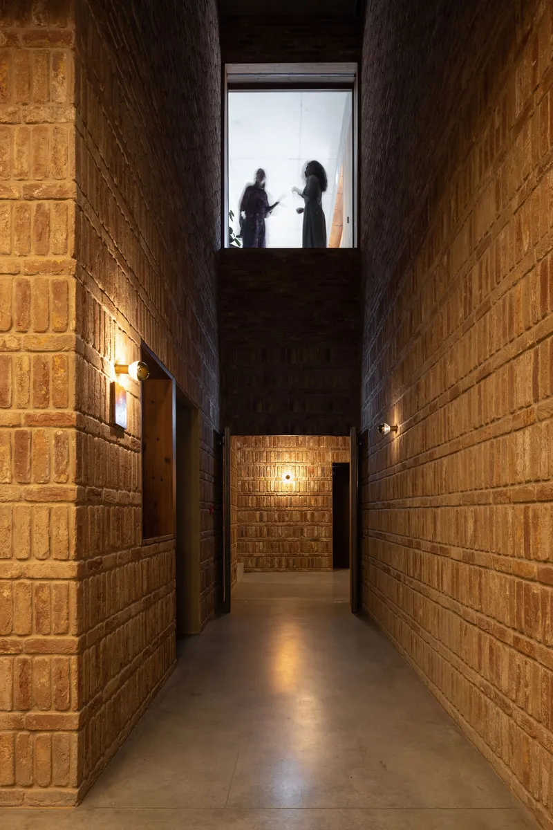 Narrow corridor with brick walls and two figures silhouetted in the skylit opening above