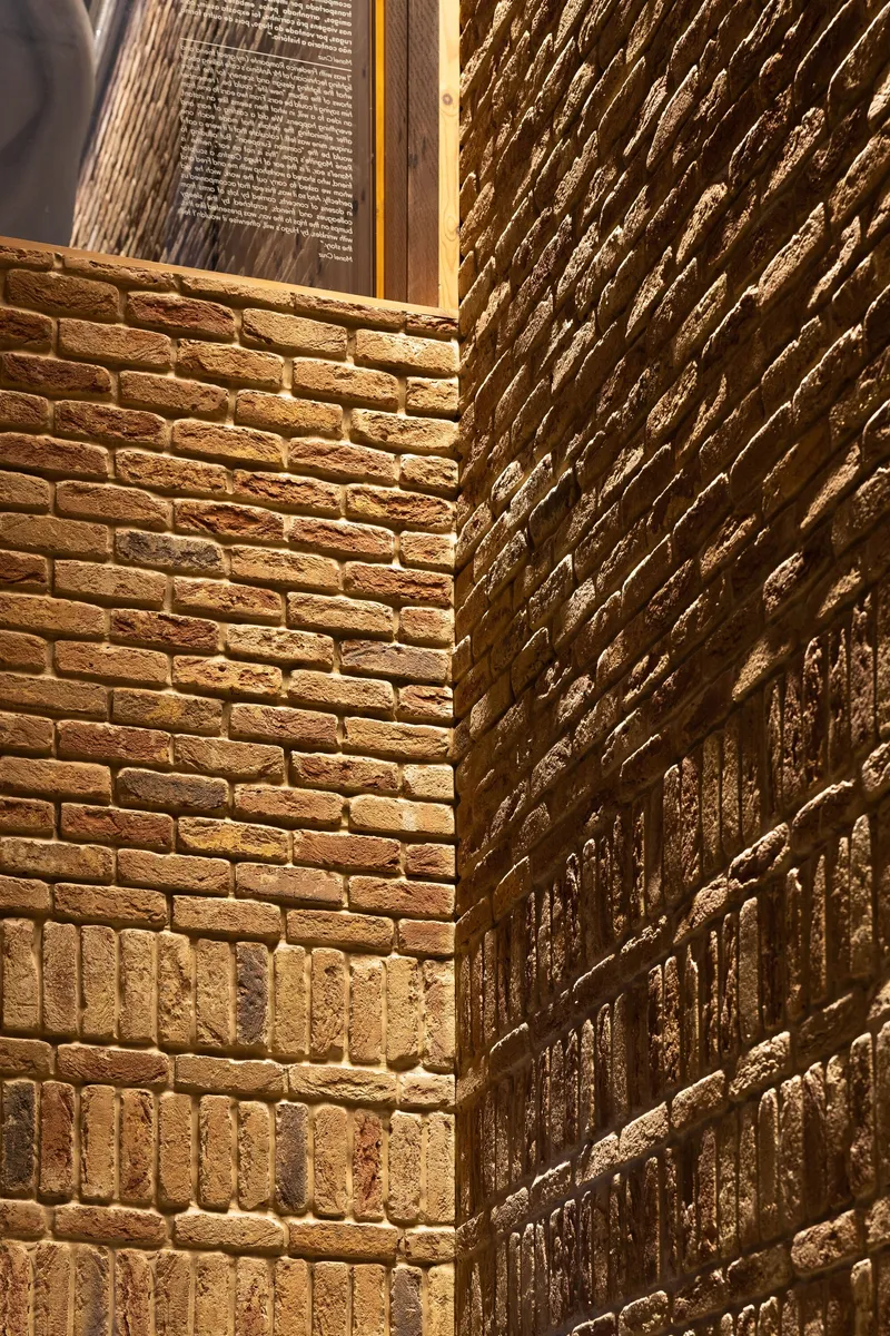 Corner detail of brick walls meeting with uplighting casting shadows on the textured surface