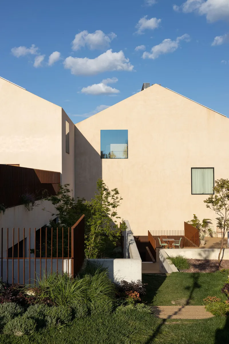 Private garden with planted beds, timber fencing and gabled volumes under a blue sky