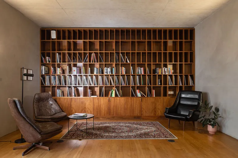 Library room with floor-to-ceiling timber shelving, two leather chairs and a patterned rug