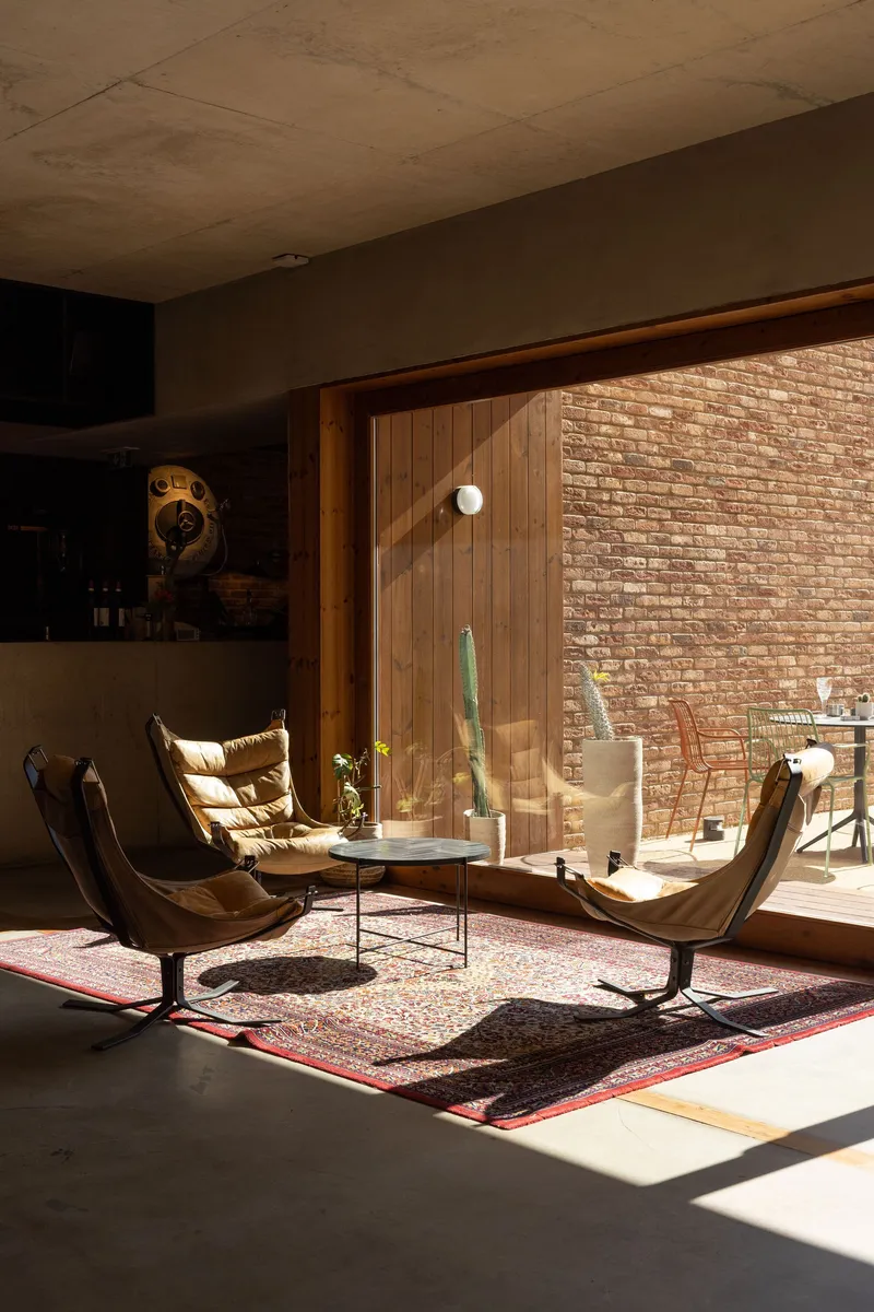 Living space with timber-clad glazing opening to a brick courtyard in afternoon sunlight