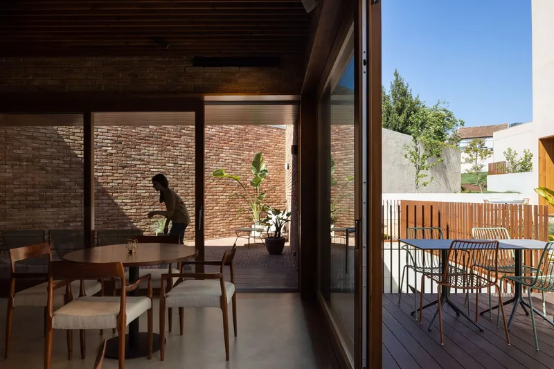 Dining area opening through glazed doors to a timber deck and brick courtyard wall