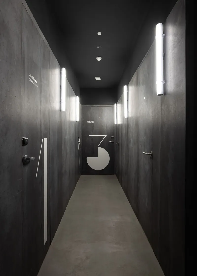 Corridor with dark timber walls, vertical light fixtures, and a graphic number three at the end