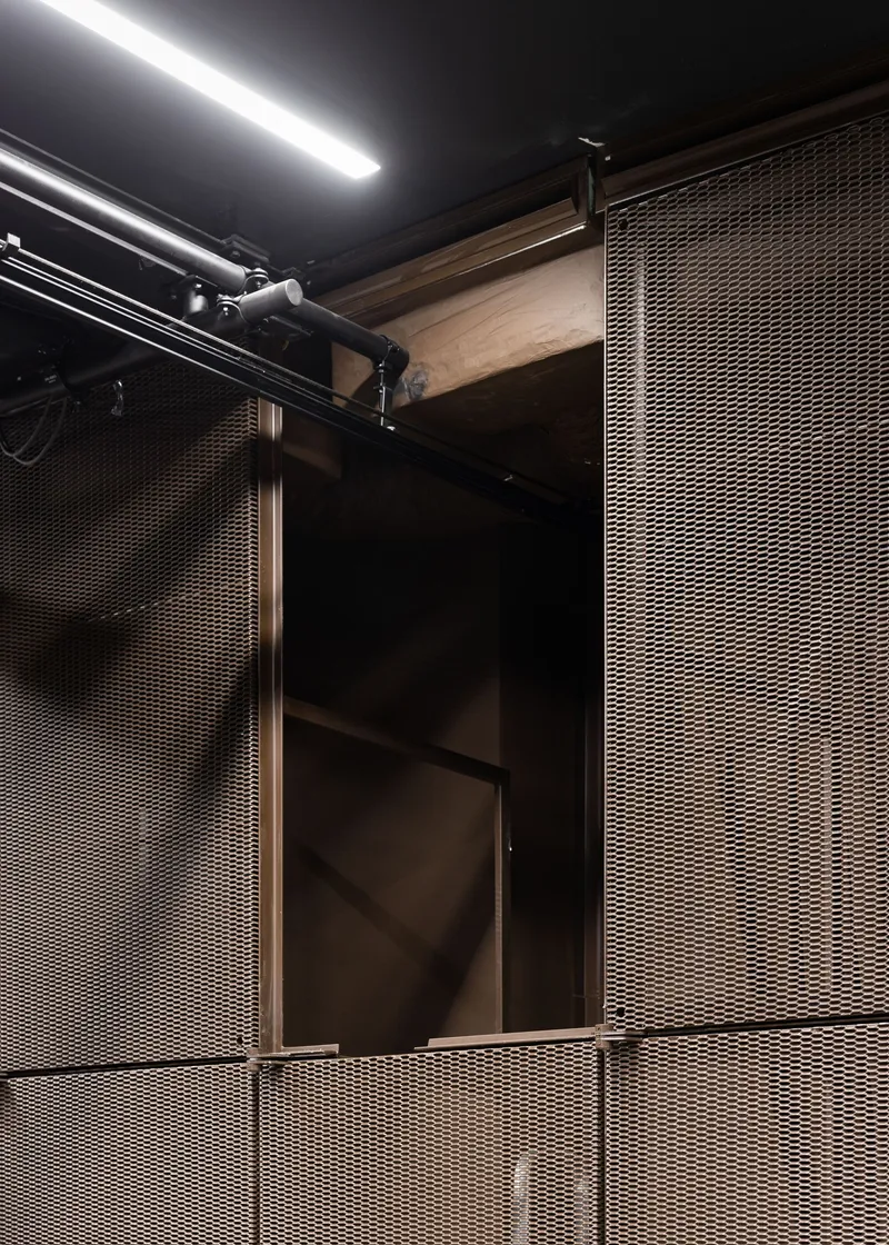 Detail of metal mesh panels meeting timber framing with track lighting overhead