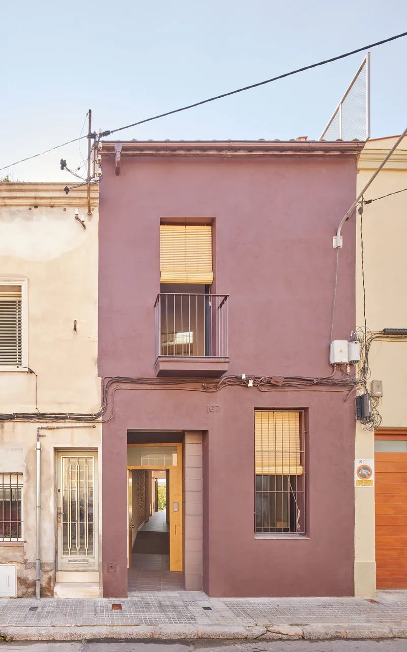 Street facade with mauve render, timber-screened openings and small balcony beneath overhead power lines