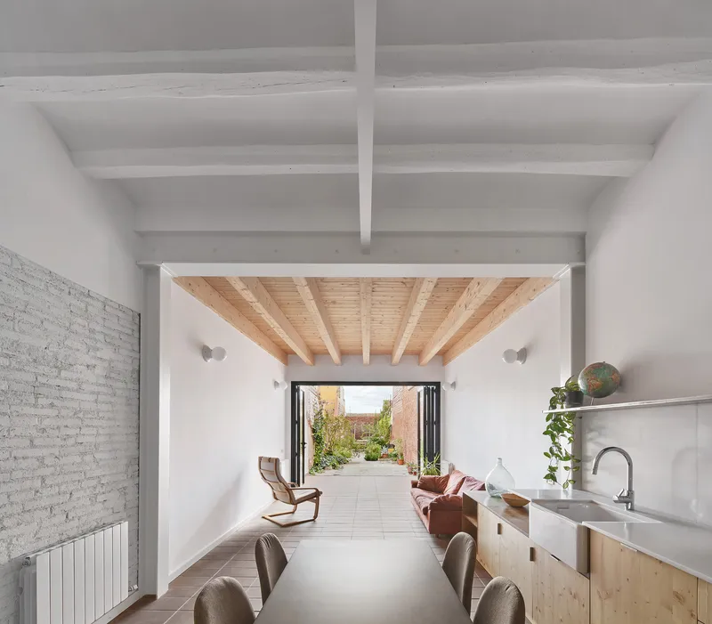 Interior view through dining and kitchen spaces toward the folding glass doors and planted courtyard beyond