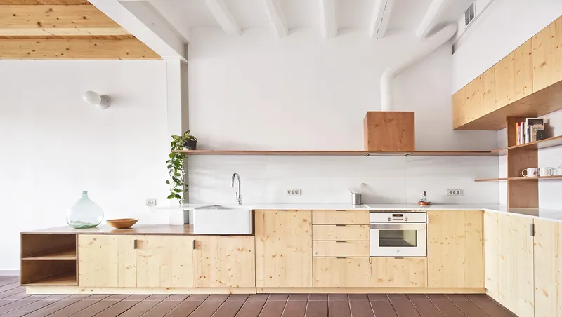 Pine plywood kitchen with farmhouse sink and exposed timber joists above dark floorboards