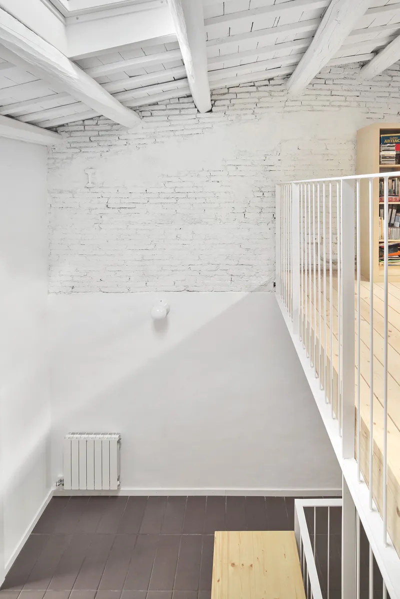 Triple-height void with whitewashed brick wall and timber beam ceiling beneath a skylight