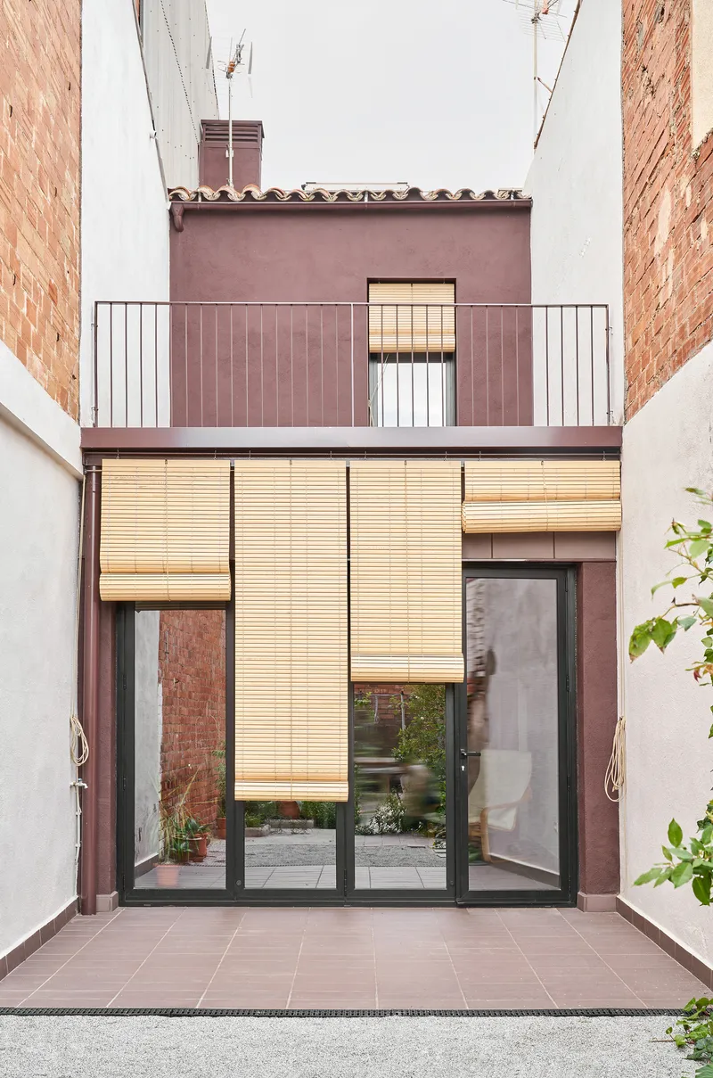 Courtyard facade with burgundy tile cladding, glazed doors, and retractable timber slatted shutters partially lowered