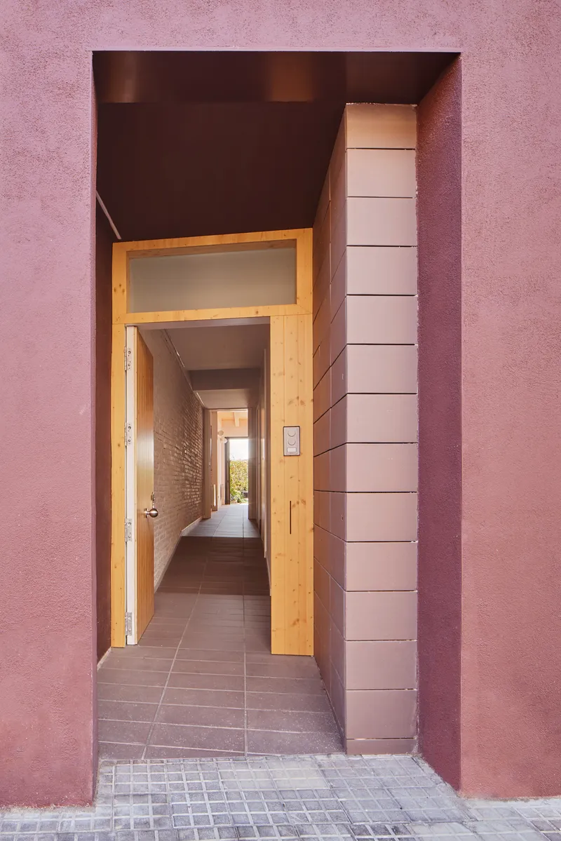 Street entrance with burgundy plastered portal framing a timber door and view into a tiled corridor