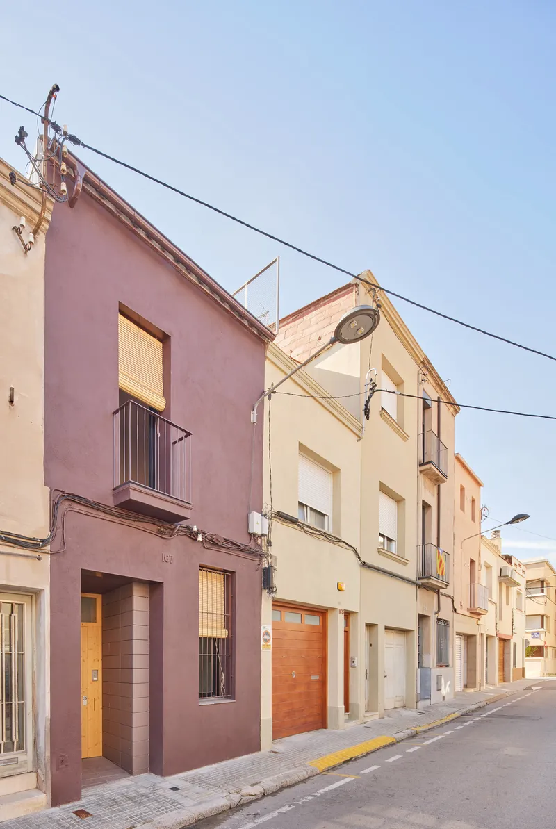 Street elevation at dusk showing the burgundy plastered facade inserted among neighboring terrace houses