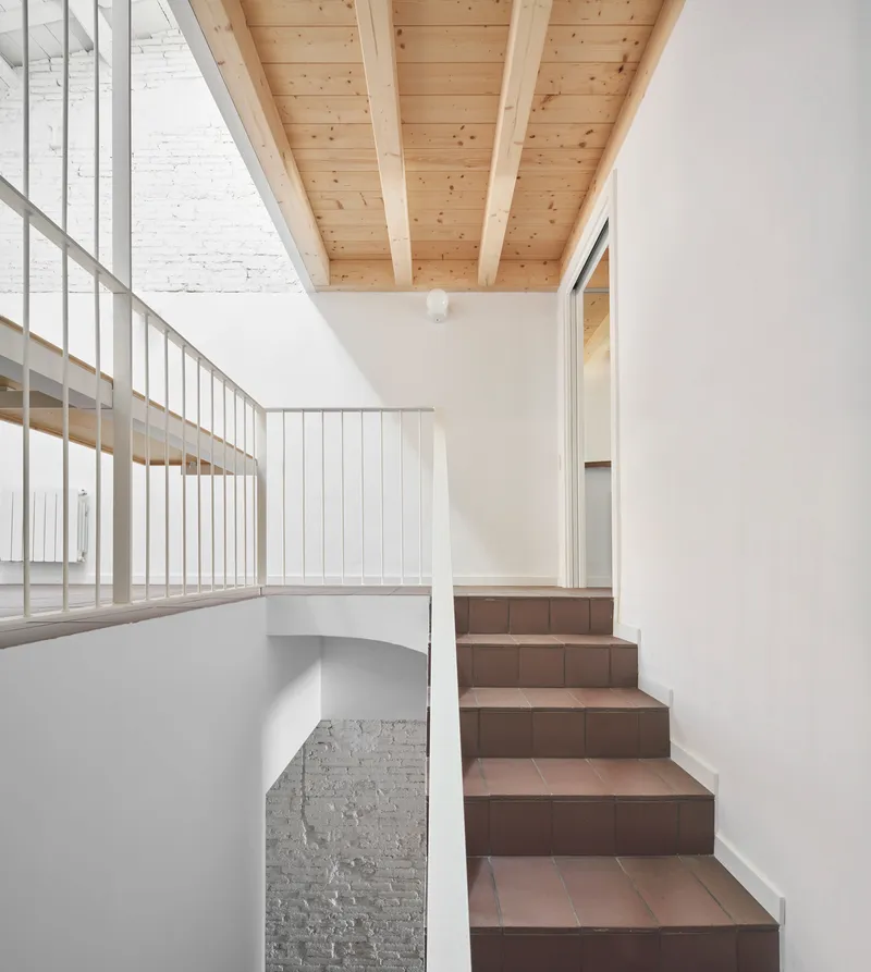 Interior staircase with terracotta treads and white metal railing beneath an exposed timber beam ceiling