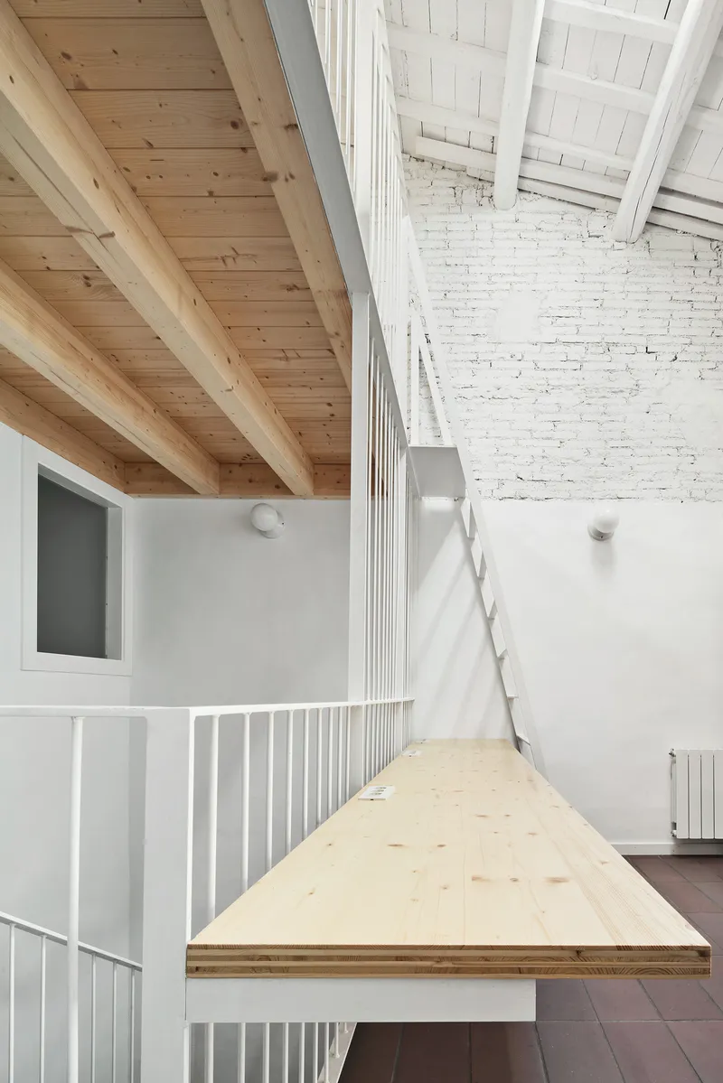 Cantilevered plywood platform with metal railing beneath exposed timber joists and painted brick walls
