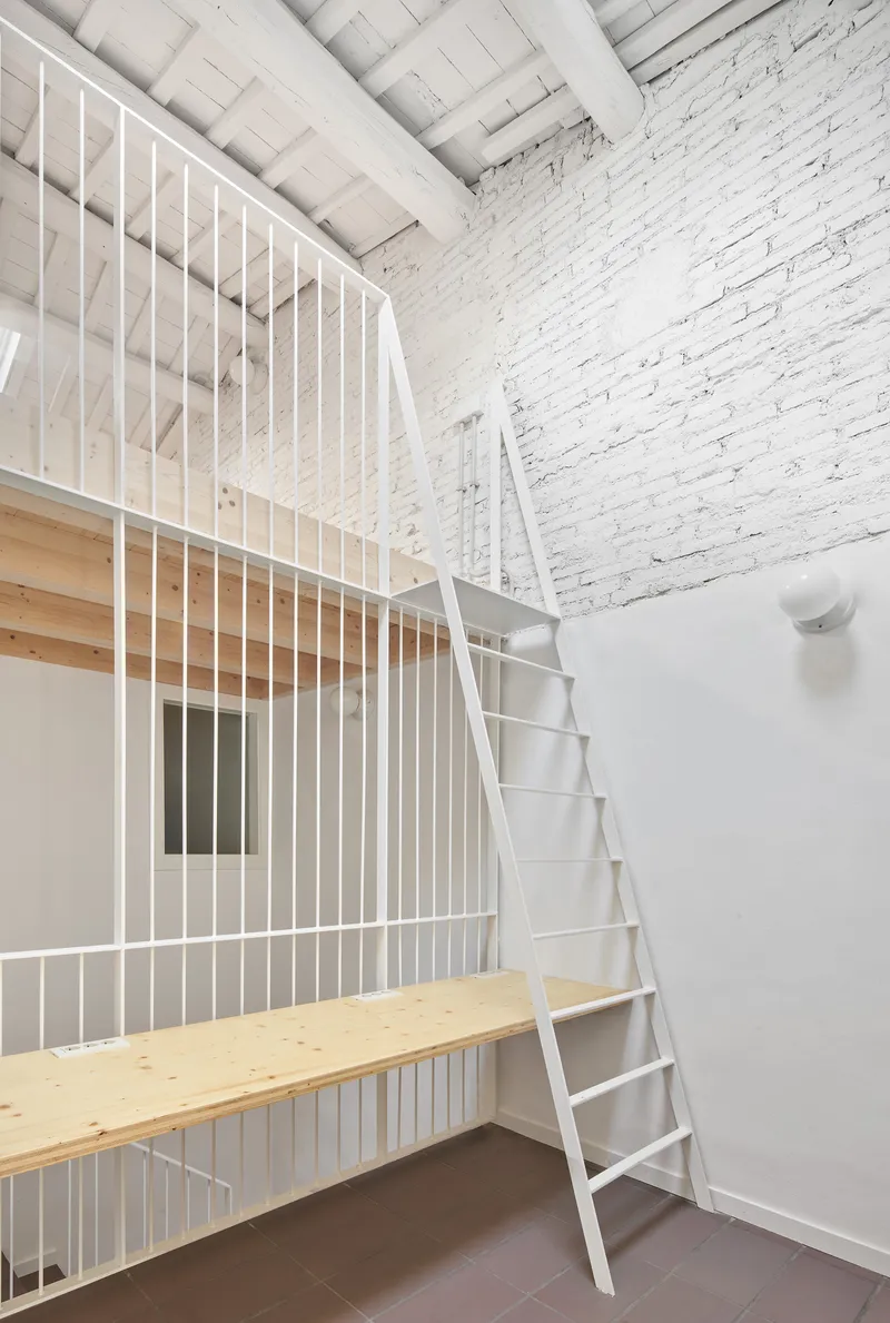 White ladder leaning against a plywood mezzanine platform with metal railing in a tall white-walled volume