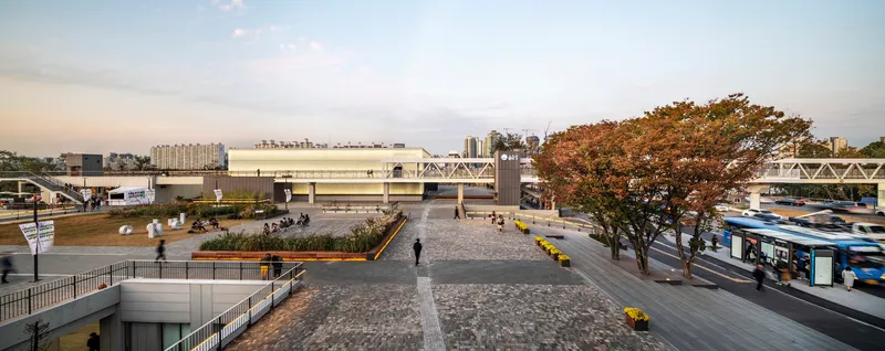 Public plaza with cobblestone paving and an autumn tree between raised transit platforms
