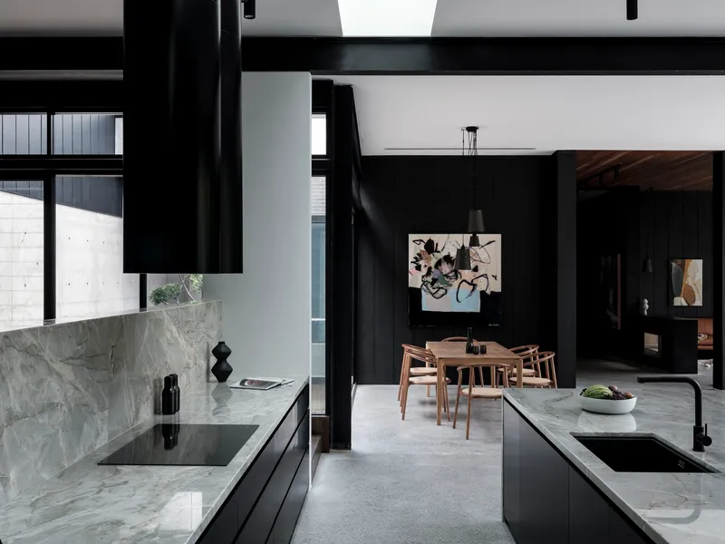 Kitchen island with grey marble countertop and timber dining table visible through black structural columns