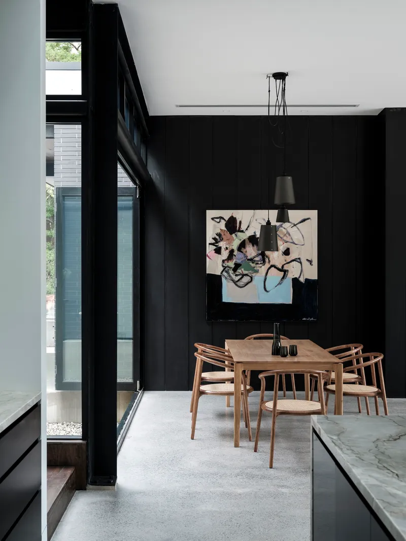 Timber dining table centered beneath black pendant lights with full-height glazing on left wall