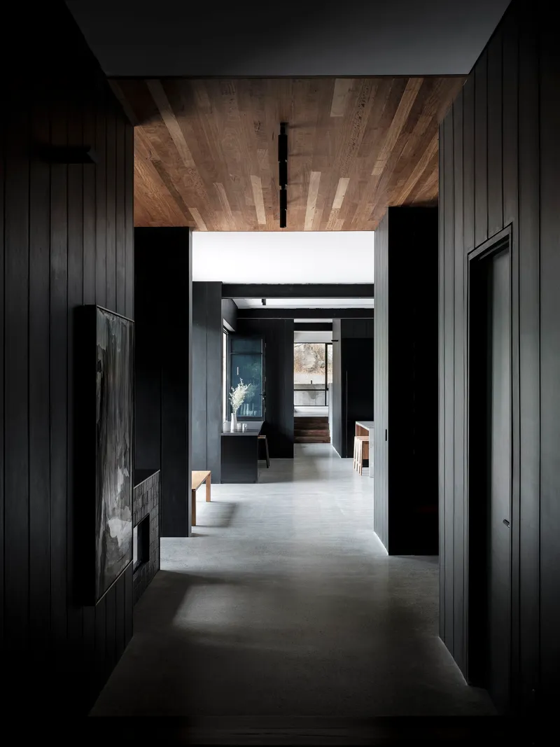 Corridor with timber plank ceiling stretching toward glazed opening with natural daylight filtering through
