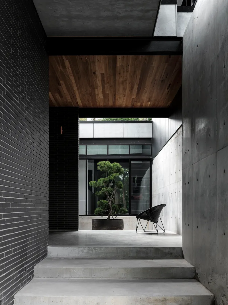 Concrete stairs ascending between black brick wall and board-formed concrete wall with timber ceiling panel overhead