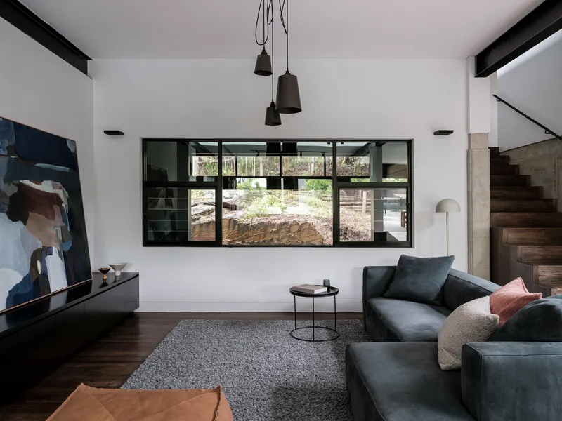 Double-height living room with black-framed window overlooking an excavated courtyard and concrete retaining wall