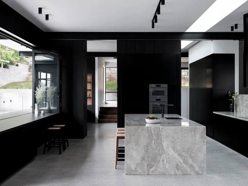 Kitchen with black paneled cabinetry and a waterfall-edge marble island under skylights